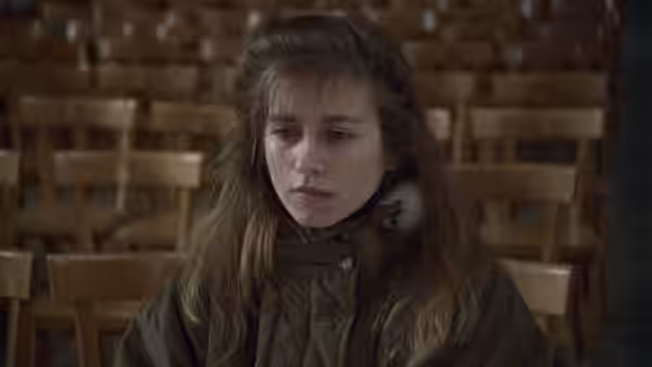 Félicie sits alone among rows of wooden chairs