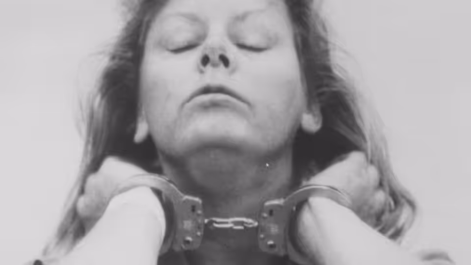 A woman with closed eyes is restrained in handcuffs as hands hold her shoulders