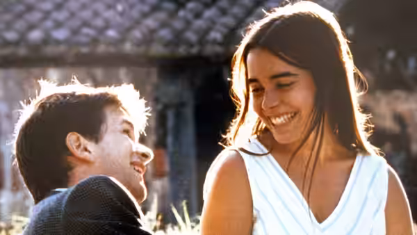 A young woman smiles down at a seated young man outside a house