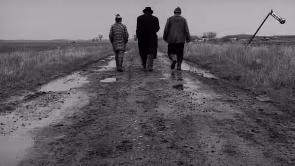 Three men walk away along a muddy country road