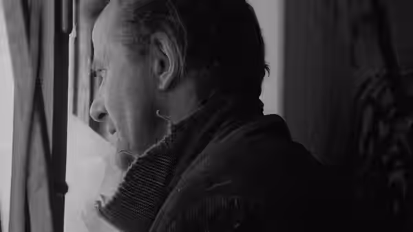 A man in a scarf looks out through a window