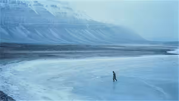 A lone bundled figure crosses a vast frozen plain beneath steep mountains