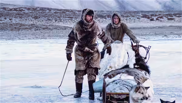 Two bundled men haul a loaded dog sled across a frozen landscape