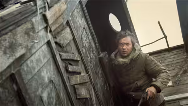 A bundled man crouches in the doorway of a weathered hut, holding a rifle