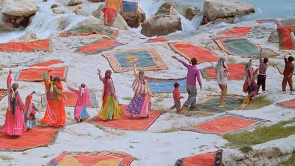 Women and children spread colorful carpets across rocks beside a rushing stream