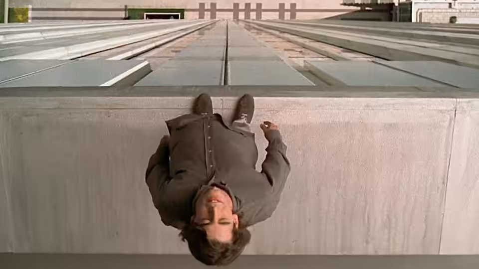 César (Eduardo Noriega) hangs upside down over a rooftop ledge