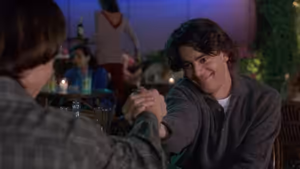 César (Eduardo Noriega) clasps hands with a man across a café table