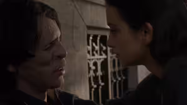César's scarred face is inches from Sofía's as they look at each other by a window