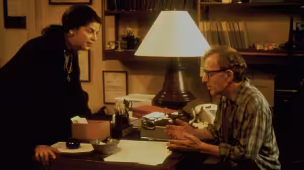 Harry (Woody Allen) gestures across a desk toward a dark-haired woman