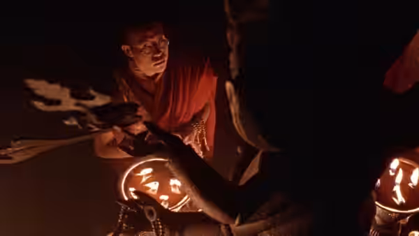 A monk leans over a lit ritual lamp during a ceremony