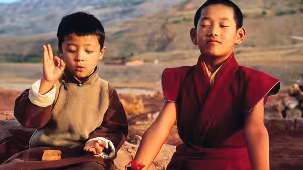 Two young monks sit outdoors as one meditates and the other rests with eyes closed