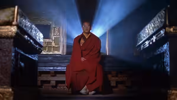 The adult Dalai Lama sits alone on a raised platform between ornate temple furnishings