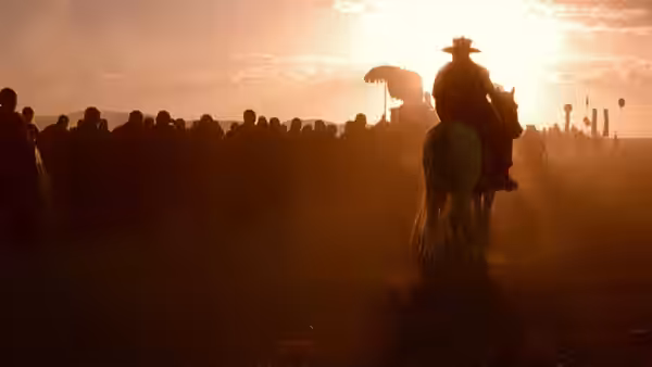 A rider on horseback approaches a crowd gathered in the sunset