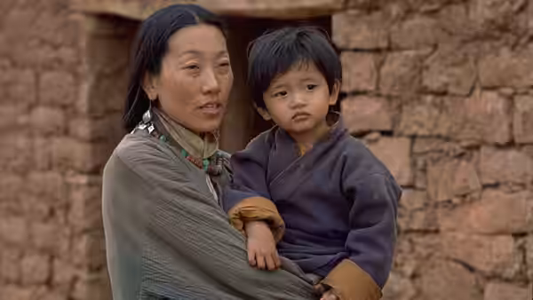 A woman holds a young child outside a stone building