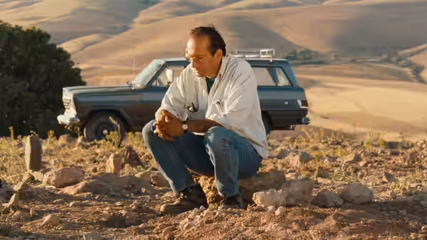 Behzad (Behzad Dorani) crouches beside his parked car on rocky ground