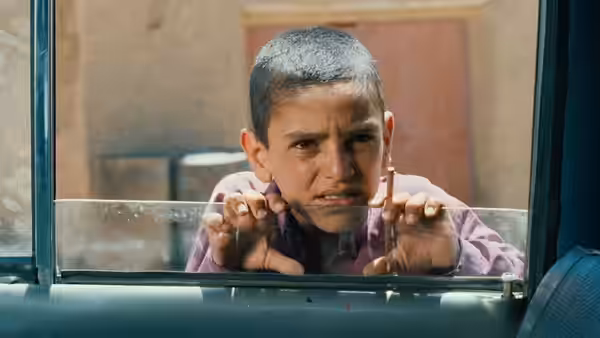 A boy grips a car window and peers inside