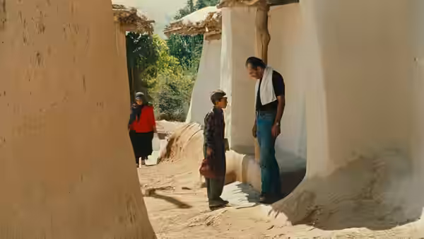 Behzad (Behzad Dorani) talks with a boy in a narrow village lane
