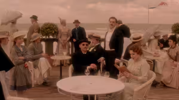 Baron de Charlus (John Malkovich) sits among guests at a seaside café