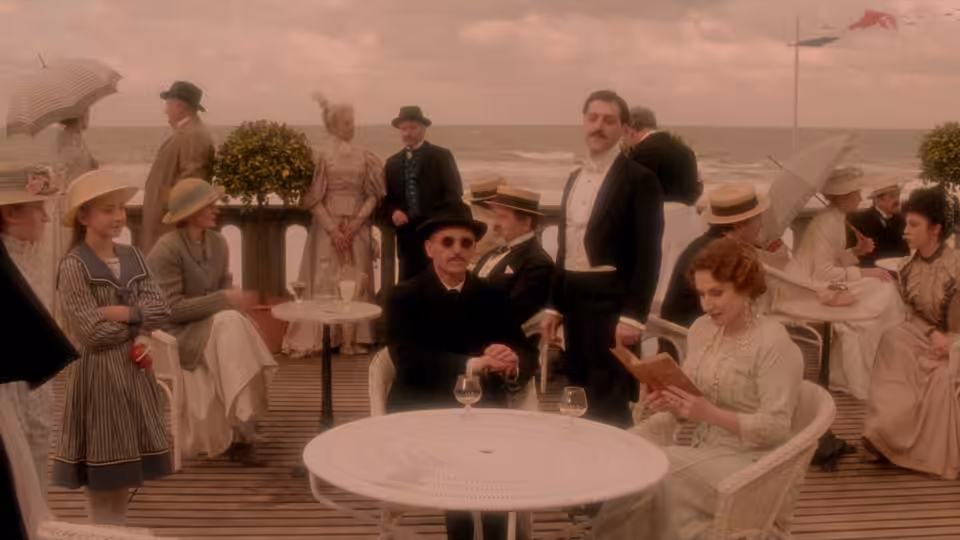 Baron de Charlus (John Malkovich) sits among guests at a seaside café