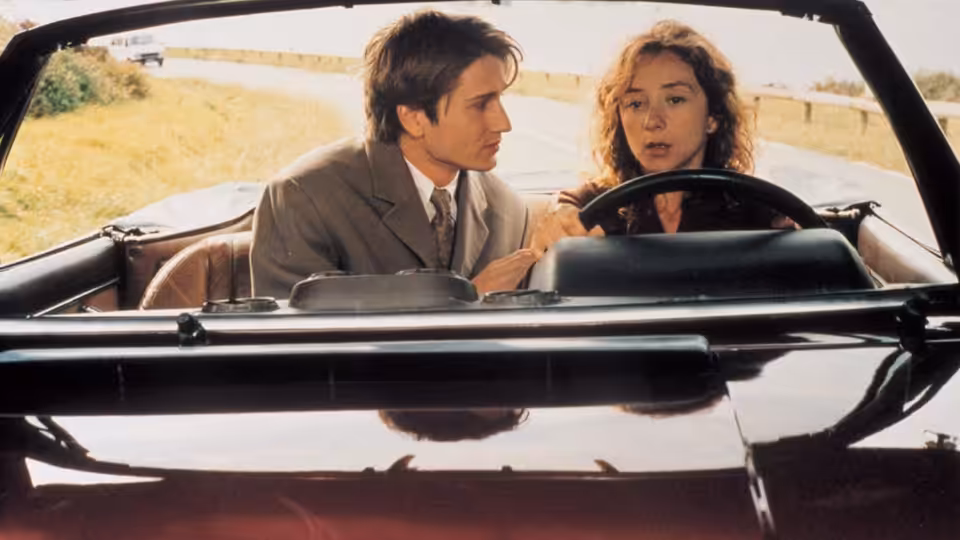 Simon (Stanislas Merhar) leans toward Ariane (Sylvie Testud) as she sits behind the wheel of a convertible