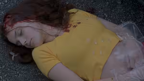 Elena (Roxane Mesquida) lies wounded on pavement in a yellow blouse