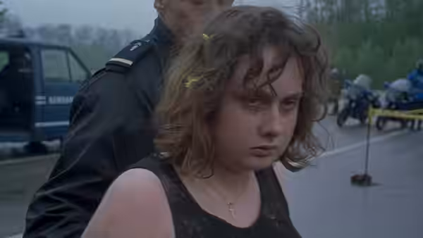 Anaïs (Anaïs Reboux) stands beside a uniformed officer at a roadside scene