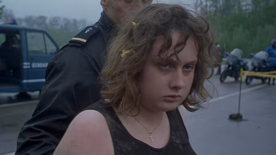 Anaïs (Anaïs Reboux) stands beside a uniformed officer at a roadside scene
