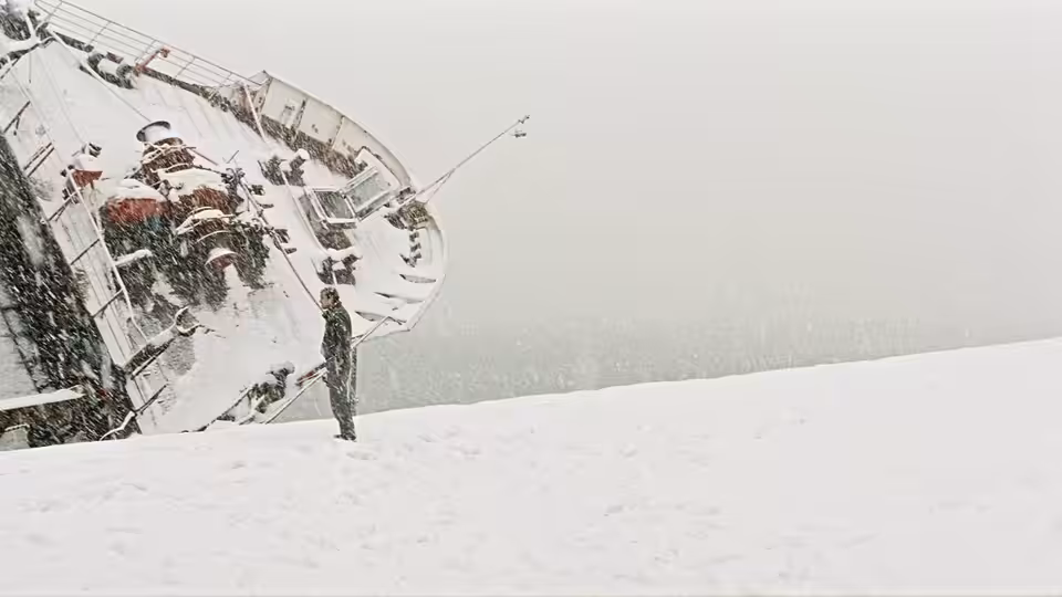 A man stands beside a stranded ship on a snow-covered shore