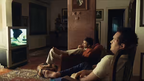Two men sit in an apartment watching television