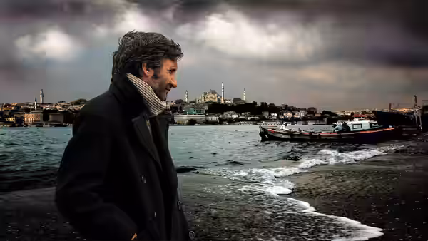 A man in a dark coat looks out over the waterfront and boats