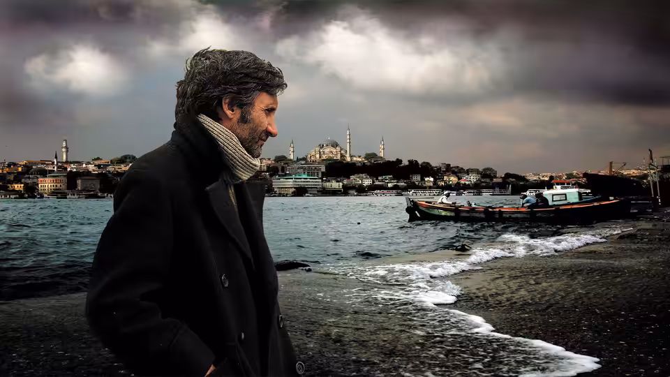 A man in a dark coat looks out over the waterfront and boats