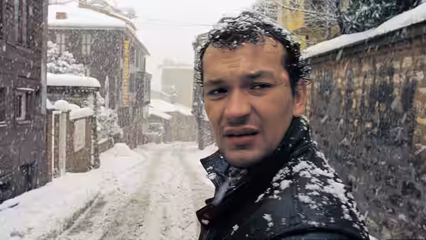 A man in a snow-covered coat turns in a narrow, snowy alley