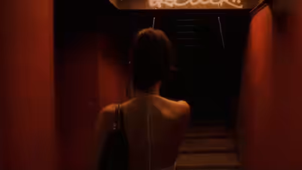 A woman approaches a staircase from a red-lit corridor