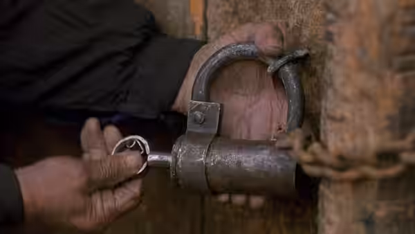 Hands unlock a heavy padlock securing a chain