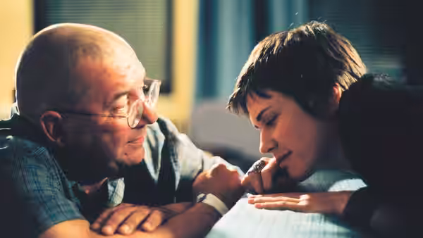 Rémy (Rémy Girard) gently holds Nathalie’s (Marie-Josée Croze) hand indoors
