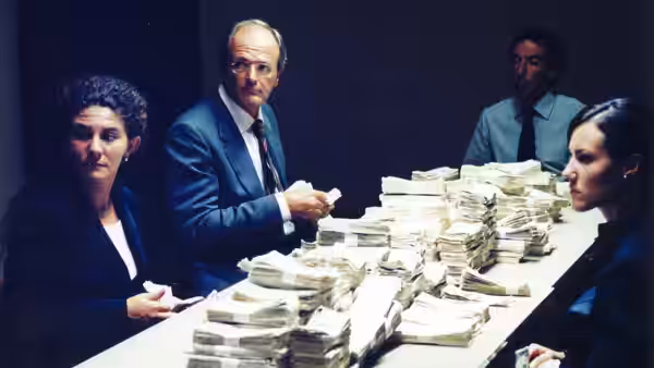 Bank employees sit around a table piled high with bundled cash