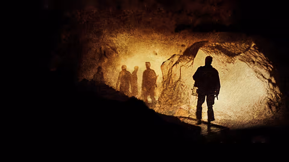Silhouetted visitors stand inside a cave beside a brightly lit passage