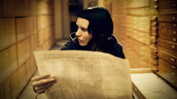 Lisbeth Salander (Rooney Mara) reads a newspaper among rows of archive drawers