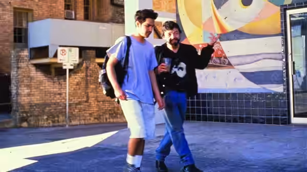Two young men walking past a colorful mural on a city street