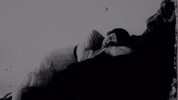 A woman reclines on a rocky outcrop, resting her head on her folded arms