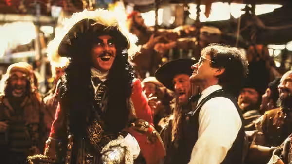Captain Hook (Dustin Hoffman) laughs beside Peter Banning (Robin Williams) among a pirate crew