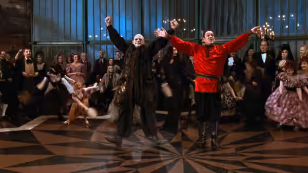 Uncle Fester (Christopher Lloyd) and Gomez Addams (Raul Julia) dance with arms raised in a hall