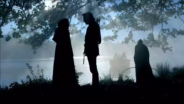 Silhouettes of people standing by a lake under misty trees