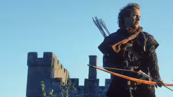 Robin Hood (Kevin Costner) holding a bow in front of a castle