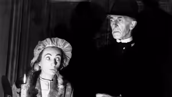 Minnie (Una O'Connor) holds a lit candle beside a man in uniform