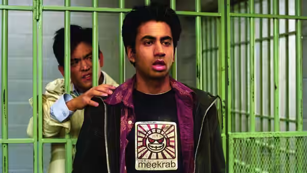 Kumar (Kal Penn) stands behind bars as Harold (John Cho) reaches toward him
