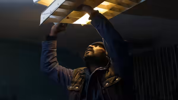 Dheepan (Antonythasan Jesuthasan) reaches up to repair a ceiling light in a dim room