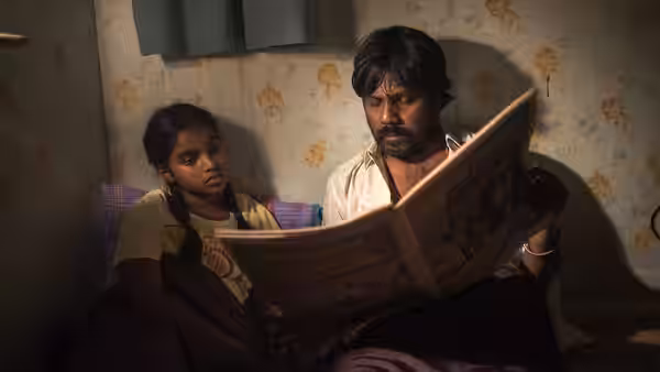 Dheepan (Antonythasan Jesuthasan) reads a newspaper beside Illayaal (Claudine Vinasithamby) in a small bedroom