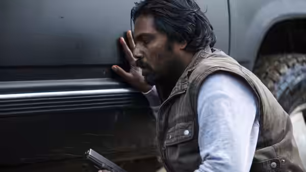Dheepan (Antonythasan Jesuthasan) leans against a vehicle while holding a handgun
