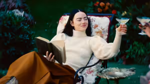 woman in white sweater reclining in garden chair holding book and glass